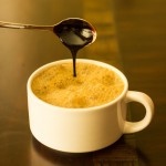 Cup of hot soymilk with molasses being drizzled in from a spoon