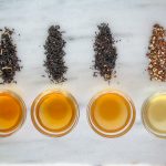 5 cups of brewed tea next to piles of loose tea