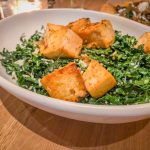 A round white bowl filled with kale and cubes of browned tofu