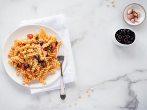 Plate of pasta with a fork and two small bowls of garlic and olives