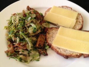 Plate with tofu and brussels sprouts next to bread with cheese