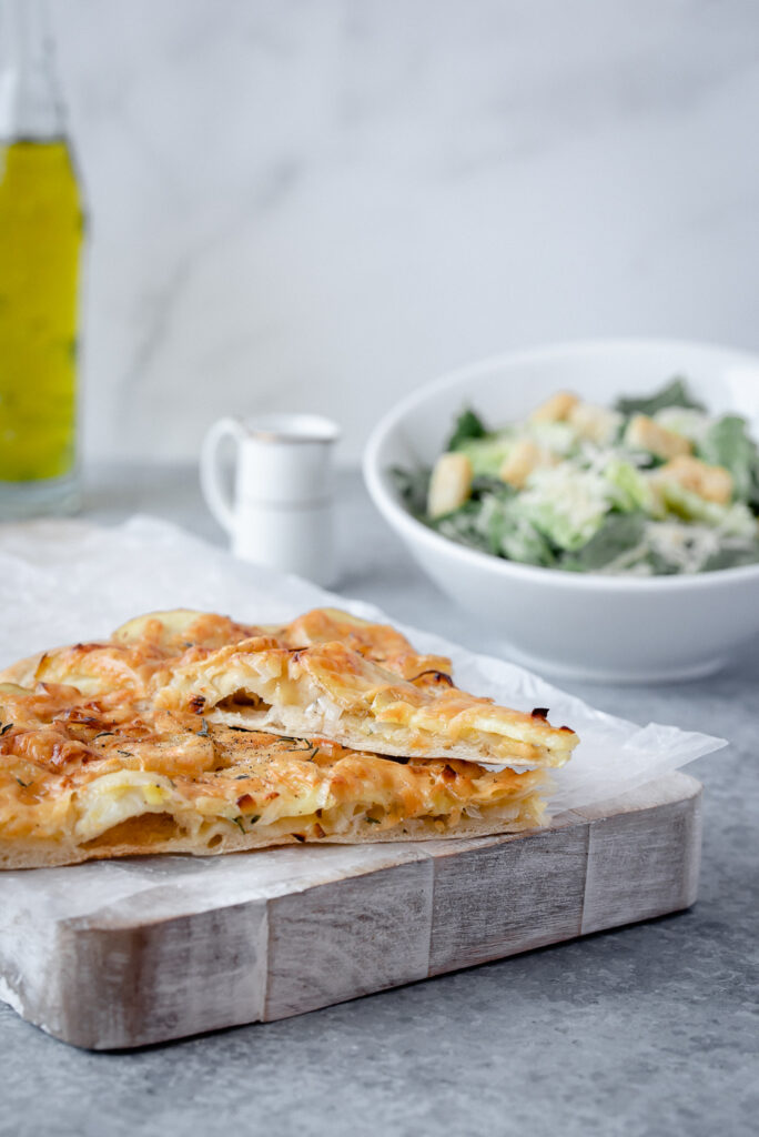 Two slices of pizza on a cutting board with salad in the background