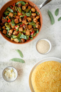 Top down view of skillet of stir fry and a round noodle cake