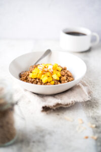 Bowl of hot cereal with mango next to a cup of coffee