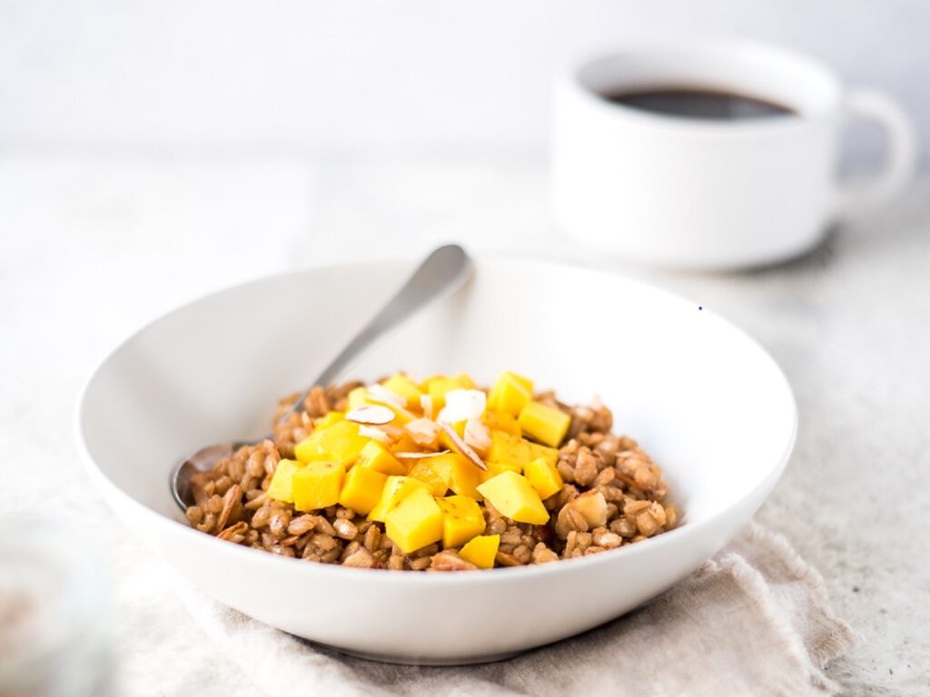 Bowl of cooked barley next to a cup of coffee