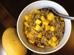 White bowl filled with hot cereal and mango chunks next to a whole mango