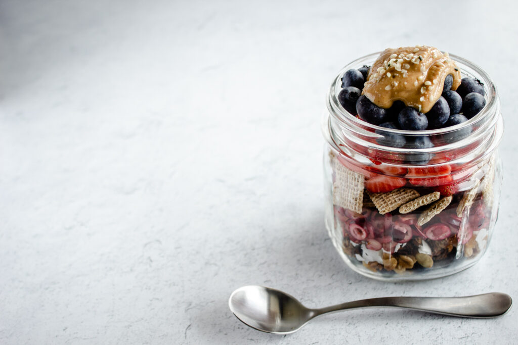 Short mason jar filled with layers of cereal and fruit