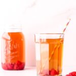 Cup of iced tea with raspberries and a straw in front of a mason jar of iced tea