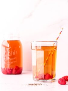 Cup of iced tea with raspberries and a straw in front of a mason jar of iced tea