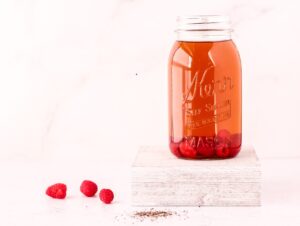 Mason jar filled with iced tea and raspberries on a white background