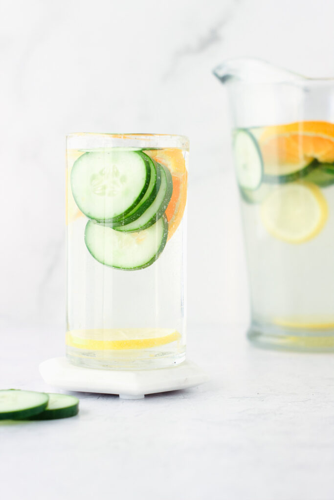 Glass of water and pitcher of water with cucumber and citrus slices