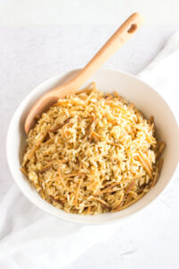 Angled down view of a white bowl with rice and a wooden spoon