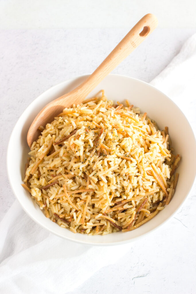 Angled down view of a white bowl with rice and a wooden spoon