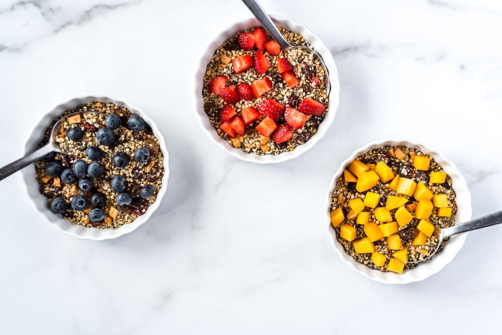 Three bowls of seeds and dried fruit cereal topped with fresh fruit