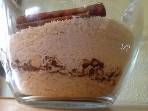 Rice, almonds, coconut and cinnamon sticks layered in a glass measuring cup