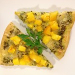 Two slices of pesto pizza on a plate with fresh tomatoes