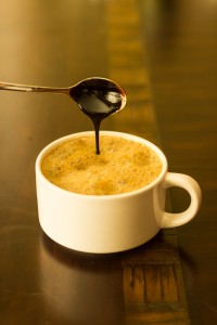 Cup of hot soymilk with molasses being drizzled in from a spoon