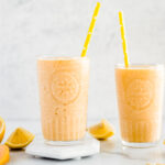 Two glasses of peach smoothie with cut lemons and peaches
