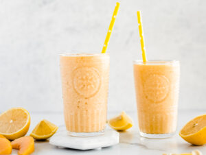 Two glasses of peach smoothie with cut lemons and peaches