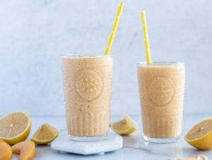 Two glasses full of peach smoothie with cut up lemons