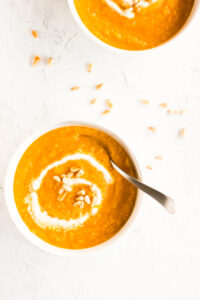 Top down view of two bowls of carrot soup with a white swirl of pine nut cream and pine nut garnish