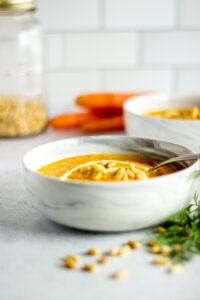 Bowl of carrot soup, jar of pine nuts, bunch of carrots