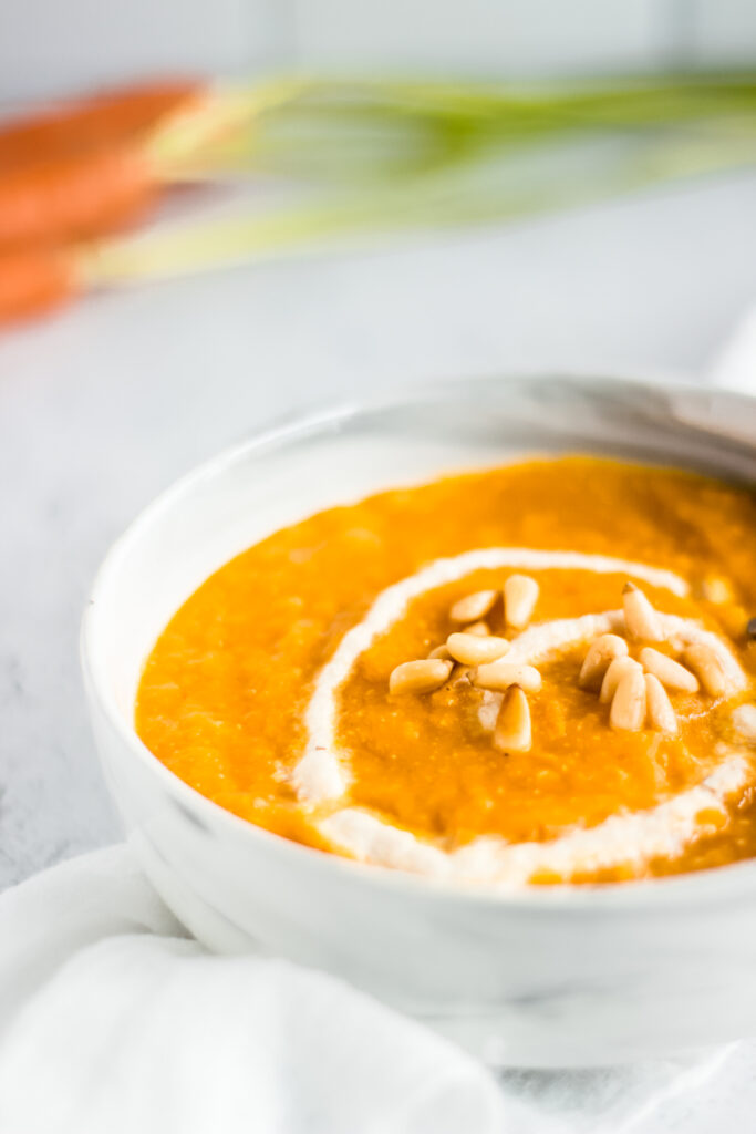 Close up view of a bowl of carrot soup garnished with pine nuts