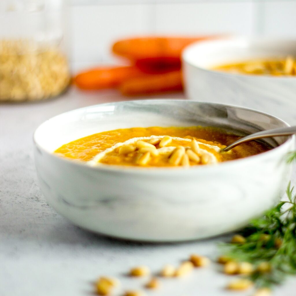 Bowl of carrot soup, pine nuts, bunch of carrots