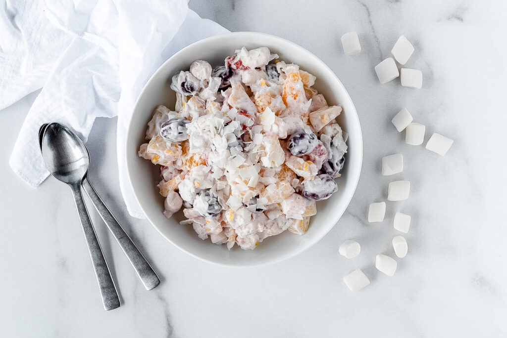 Top down view of a bowl of ambrosia next to some mini marshmallows