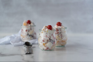 Three small jars of fruit salad with red cherry on top