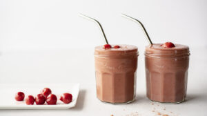 Two small jars of chocolate smoothie with straws next to a plate of cherries