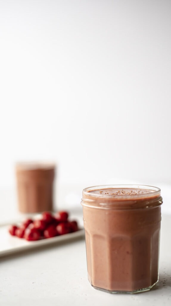 two small glasses of chocolate cherry smoothie next to a plate of cherries