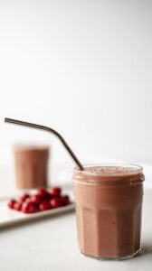 Small glass jar of smoothie with metal straw next to a plate of cherries