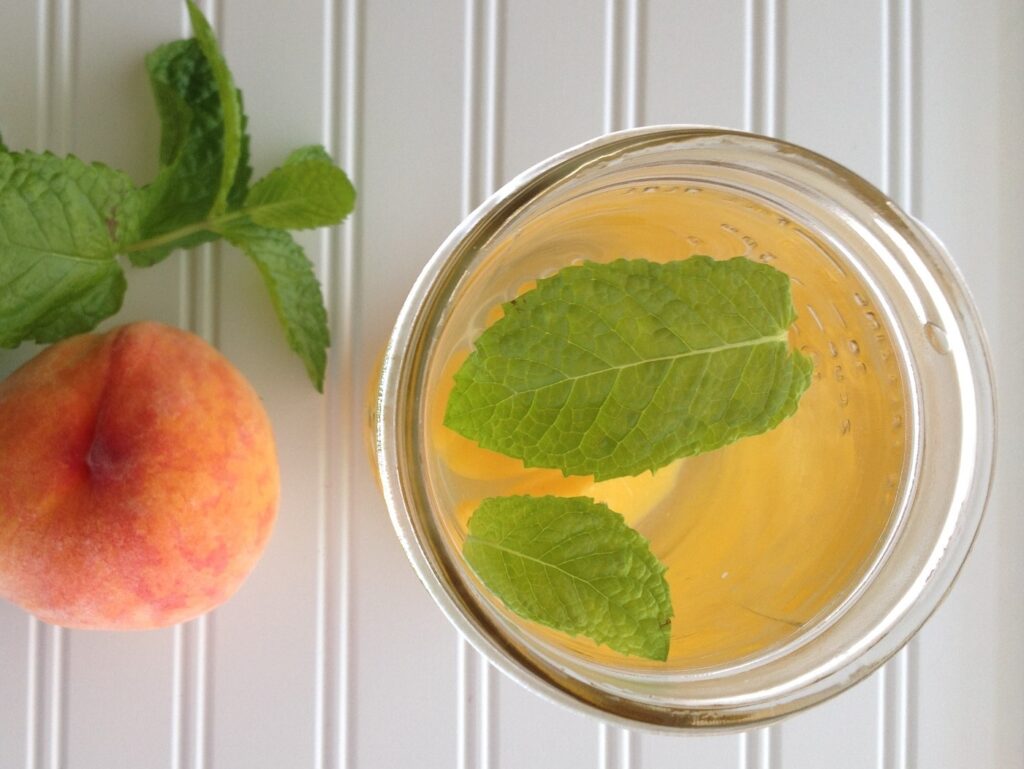 Top down view of canning jar with water flavored with fresh peach and mint leaves