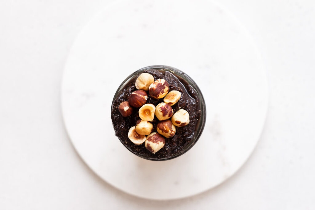 Top down view of jar of homemade nutella topped with hazelnuts