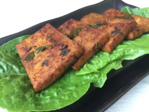 Pieces of cooked tofu on lettuce leaves on a rectangular plate