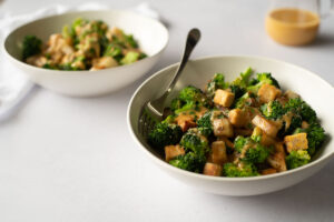 Two white bowls filled with broccoli, tempeh and potatoes