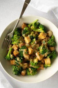 Top down view of white bowl filled with broccoli, tempeh and potatoes