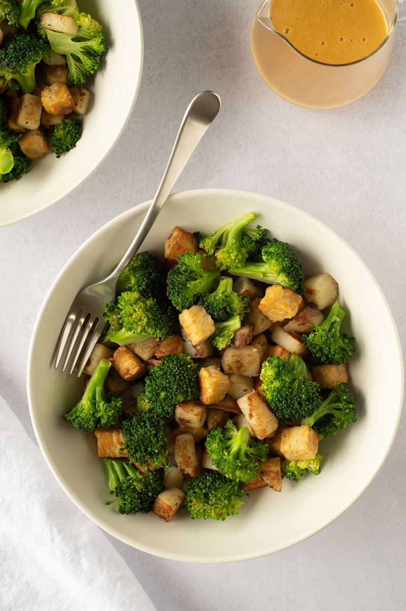 Top down view of two white bowls full of veggies and a pitcher of cheese sauce