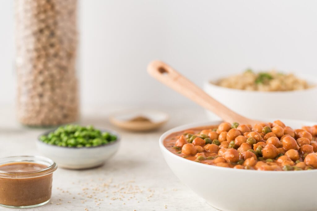 Bowl of garbanzo beans in tomato sauce with a wooden spoon to serve