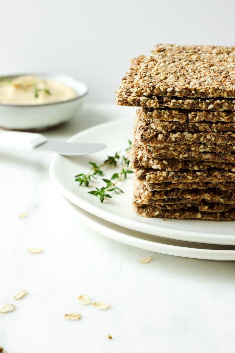 Stack of crackers on a plate next to a bowl of hummus