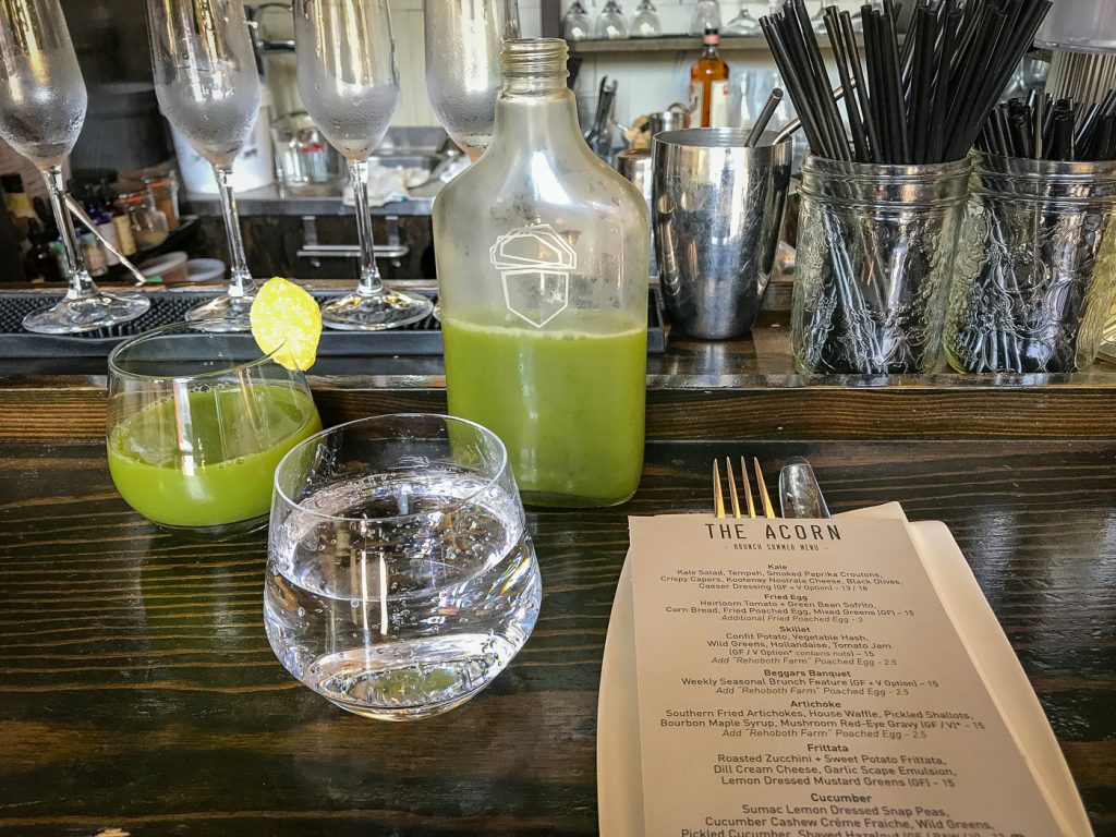 Bottle of green juice, glass of water and glass of juice on a bar