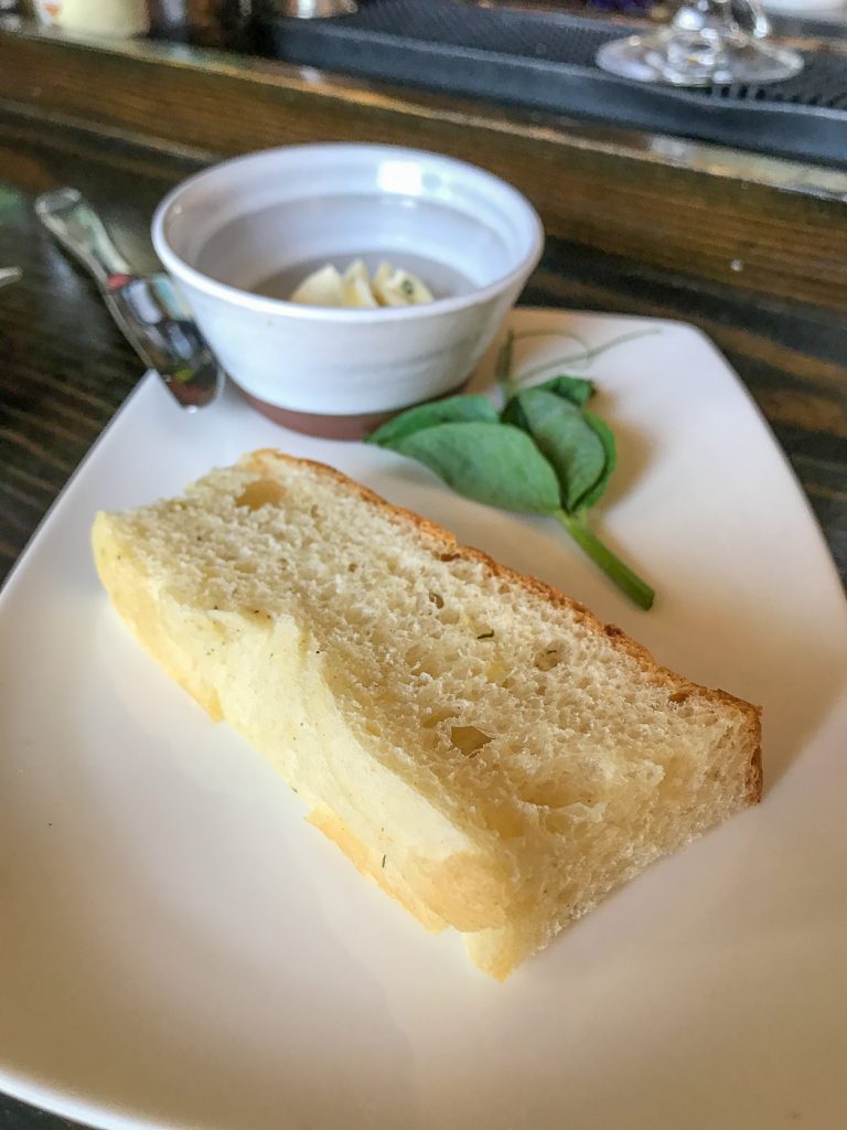 A plate with a slice of bread, and a small bowl of compound butter with a knife