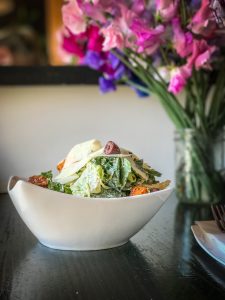 A white bowl filled with kale and cheese on a bar