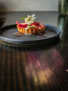 A round black plate with a small fruit tart topped with an edible flower