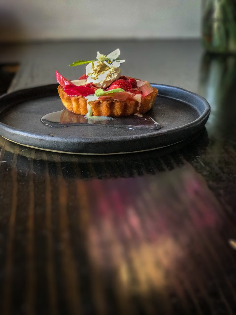 A round black plate with a small fruit tart topped with an edible flower