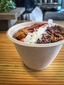 A small smoothie bowl topped with coconut, cocoa nibs, strawberries, and seed butter