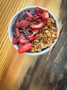 A smoothie bowl in a small cup topped with strawberries, goji berries, and granola