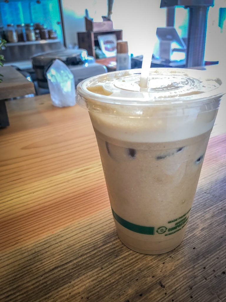 A coffee looking drink in a plastic cup on a wooden counter