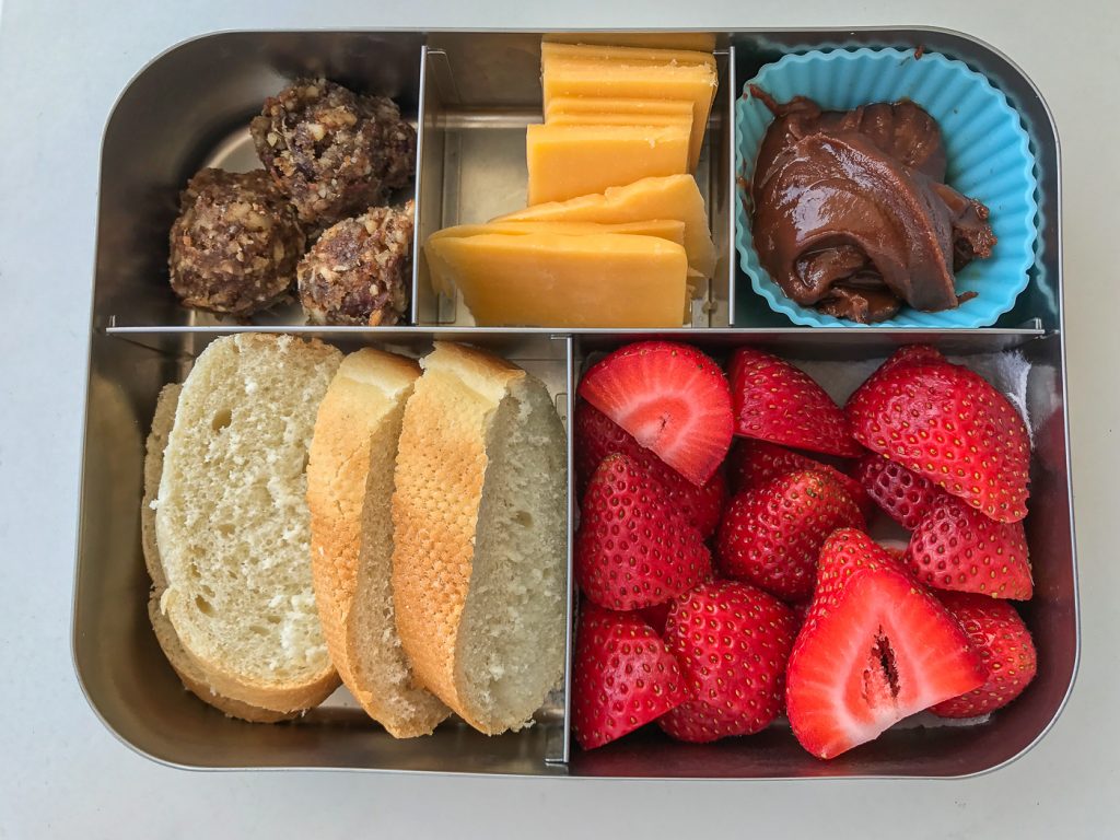 A bento lunch box filled with bread, strawberries, cheese, hazelnut spread and Unwrapp'd dough balls